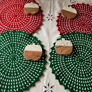 May include: Four crocheted placemats in red and green with white polka dots. Each placemat has a wooden apple-shaped coaster with a white marble top.
