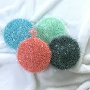 Puede incluir: Cuatro paños de cocina de ganchillo en diferentes colores: azul verdoso, verde, rosa y gris. Los paños de cocina son redondos y tienen una superficie texturizada.