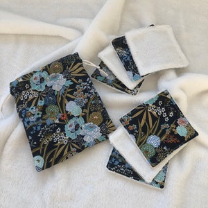 Puede incluir: Un juego de discos faciales reutilizables y una bolsa con cordón a juego. Los discos tienen un lado de rizo blanco y un lado estampado con diseños florales azules, turquesas y dorados sobre un fondo azul marino. La bolsa tiene el mismo estampado floral.