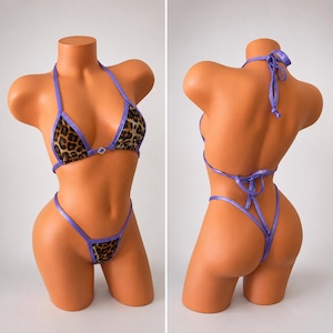 May include: A two-piece bikini set with a leopard print pattern. The bikini top and bottom are trimmed with a shiny purple material. The top is a halter style, and the bottom is a thong style. The bikini is displayed on a mannequin.