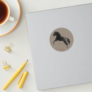May include: A black and white spotted horse with a red eye, running to the right. The horse is on a beige background with the text "G-H-H-H-M" written below it.