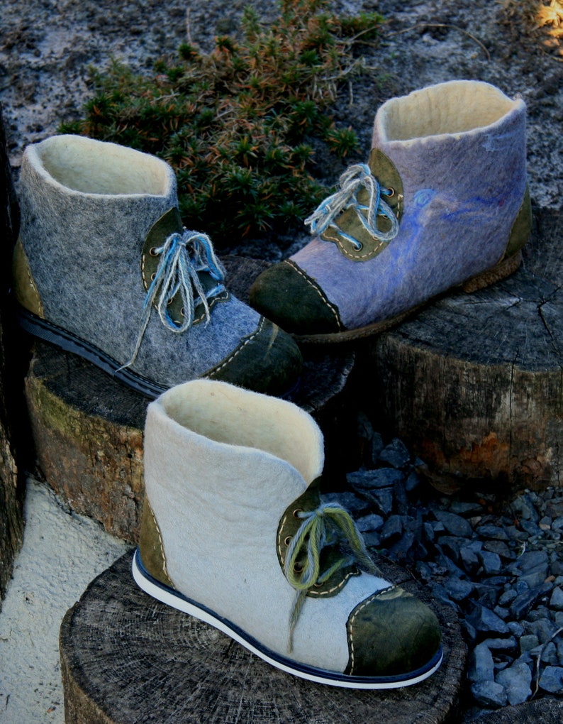 May include: Three pairs of felt boots with green and white laces. The boots are made of wool felt and have a suede toe cap. The boots are sitting on a wooden surface.