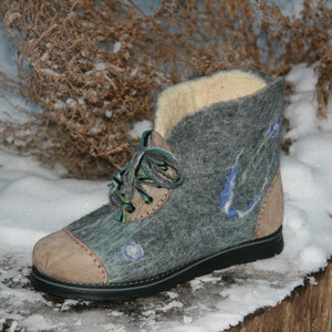 May include: Gray felt boots with a brown leather toe and blue and green laces. The boots are sitting on a snowy surface.
