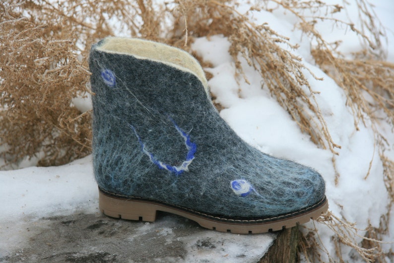 May include: A pair of blue felt boots with a white and blue design. The boots have a brown rubber sole and are sitting on a snowy surface.