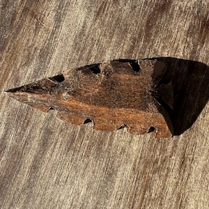 May include: A white ceramic mug with a black handle and the text "But First, Coffee" in a bold, black font. The mug is set against a blurred background, suggesting a cozy setting.
