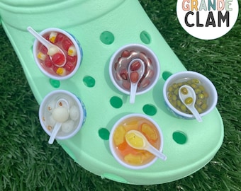 May include: A green shoe with five colorful ramen bowl shoe charms. The charms are filled with different ingredients, such as red beans, mung beans, and tapioca pearls. The shoe has the text "THE GRANDE CLAM" on the side. The text "RAMEN BOWL SHOE CHARM" is at the bottom of the image.