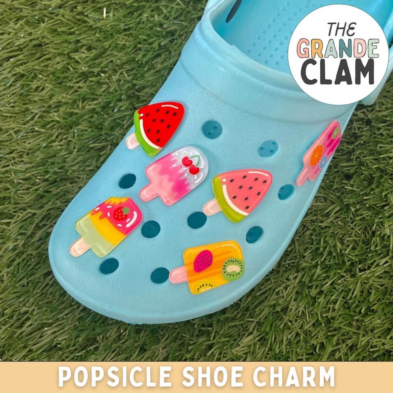 May include: Blue clog shoe with colourful popsicle shoe charms. The charms feature watermelon, strawberry, kiwi, and cherry designs. The shoe has the text "The Grande Clam" on the side.