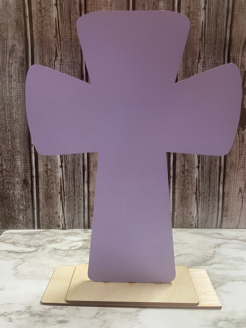 May include: A lavender wooden cross with a simple design, standing on a wooden base.