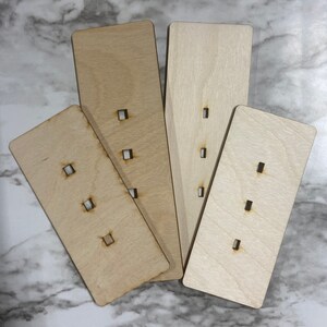 May include: Four wooden rectangular pieces with cut-out holes. The pieces are arranged in a fan shape. The pieces are light brown and have a natural wood grain.