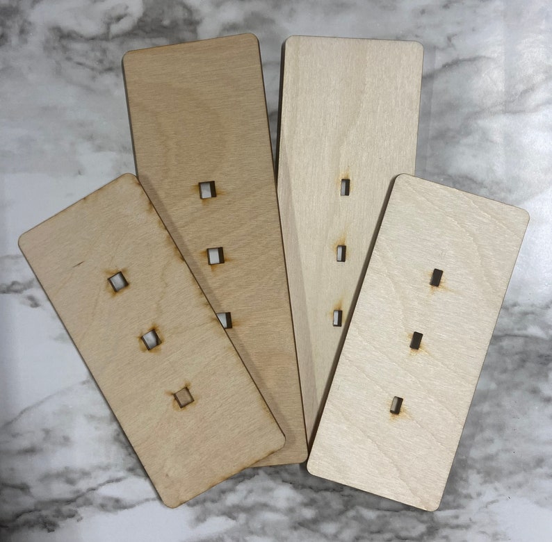 May include: Four wooden rectangular pieces with cut-out holes. The pieces are arranged in a fan shape. The pieces are light brown and have a natural wood grain.