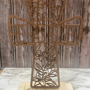 May include: A wooden cross with a floral design and the words "He Has Risen" carved into it. The cross is standing on a wooden base.