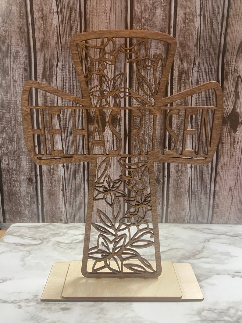 May include: A wooden cross with a floral design and the words "He Has Risen" carved into it. The cross is standing on a wooden base.