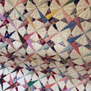 May include: A patchwork quilt featuring a repeating star pattern constructed from various multi-colored fabric scraps in shades of red, blue, yellow, green, and purple, all set against a cream-colored background with intricate fan-shaped quilting.