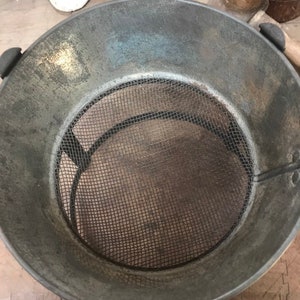 May include: A vintage metal strainer with a wire mesh bottom. The strainer is gray and has a worn, rustic look.
