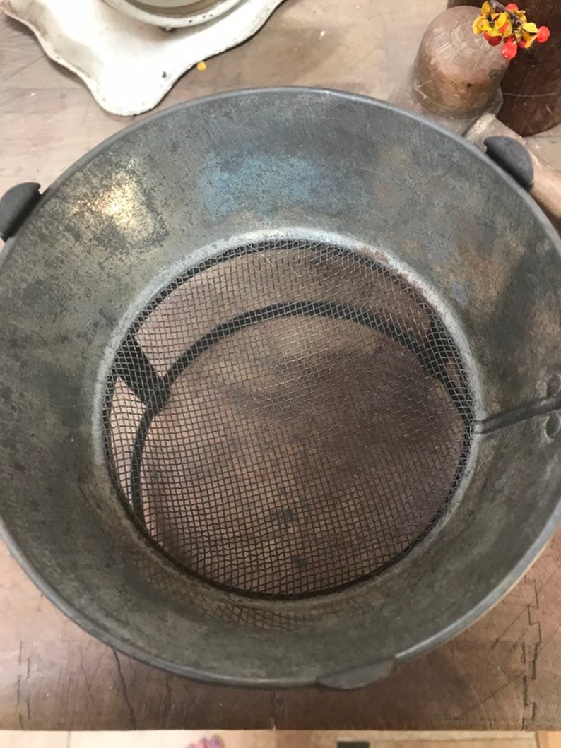 May include: A vintage metal strainer with a wire mesh bottom. The strainer is gray and has a worn, rustic look.