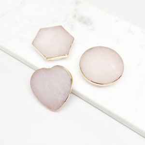 May include: Three pink phone grips with gold trim. The grips are shaped like a heart, a circle, and a hexagon.