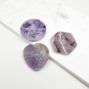 Könnte beinhalten: Drei Amethyst-Kristall-Untersetzer in verschiedenen Formen: rund, Herz und Sechseck. Die Untersetzer sind poliert und haben eine violette und weiße Farbe.