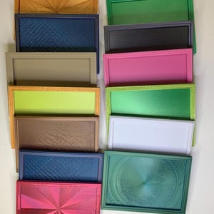 以下が含まれることがあります： オレンジ、緑、ピンク、青など、さまざまな色の長方形のトレイのコレクション。各トレイは、テクスチャ加工された表面と隆起した縁があります。幾何学模様のトレイもあれば、単色のものもあります。