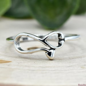 May include: A silver ring with an infinity symbol design. The infinity symbol is made of two hearts that are intertwined.