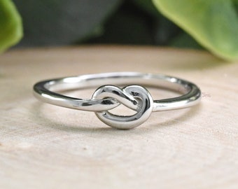 May include: A silver knot ring with a simple design. The ring is made of a thin band of metal and features a knot in the center.