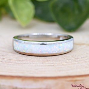 May include: A silver band ring with a white opal inlay. The ring is set on a light wood surface.