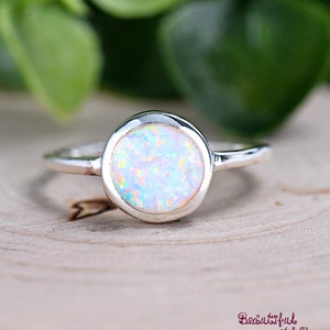 May include: A silver ring with a round white opal gemstone. The opal has a rainbow iridescent sheen.