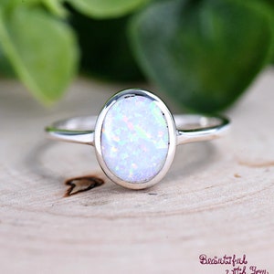May include: A silver ring with a white opal gemstone. The oval-shaped opal has a milky white color with iridescent flashes of color.