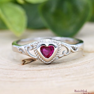 May include: A silver ring with a heart-shaped ruby gemstone set in a delicate filigree design.