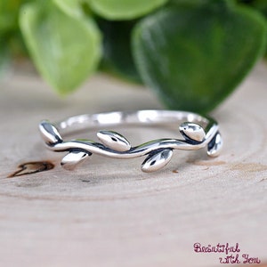 May include: A silver ring with a delicate branch design featuring small leaves. The ring is simple and elegant.