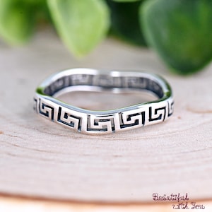 May include: A silver ring with a Greek key design. The ring is thin and has a slightly curved shape.