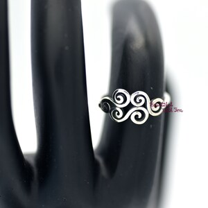 May include: Silver ring with a swirling design. The ring is on a black display stand.