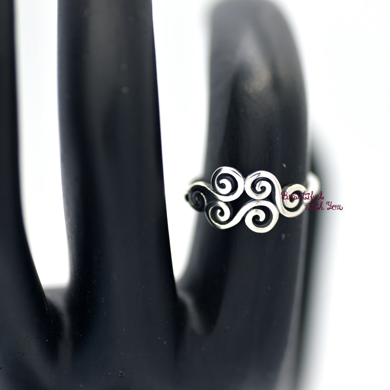 May include: Silver ring with a swirling design. The ring is on a black display stand.