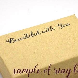 Puede incluir: Una caja de anillo de cart&oacute;n marr&oacute;n con el texto "Beautiful with you" impreso en la parte superior. Las palabras "sample of ring box" est&aacute;n impresas en la parte inferior de la caja en un tono marr&oacute;n m&aacute;s oscuro.