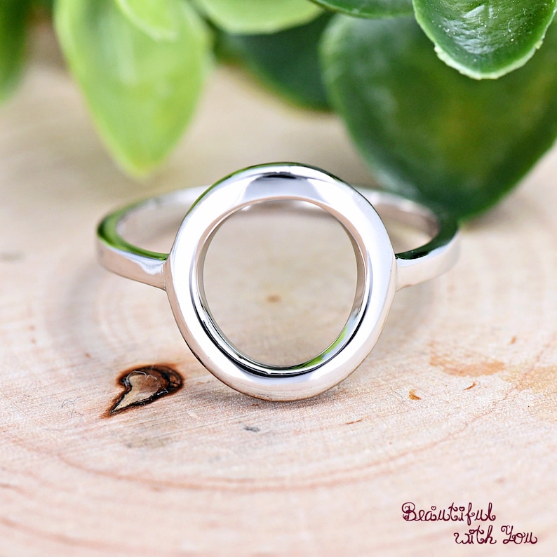 May include: A silver ring with a large, open circle design. The ring is simple and elegant.