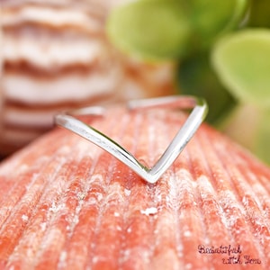 May include: A silver-colored ring with a V-shaped design. The ring is set against a textured, reddish-orange surface, with a blurred background of green and brown. The words "Beautiful with You" are in the bottom right corner.