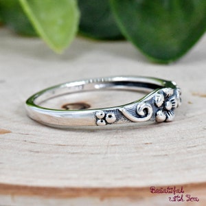 May include: A silver ring with a floral design. The ring has a delicate band with three small beads on one side and a floral design on the other side.