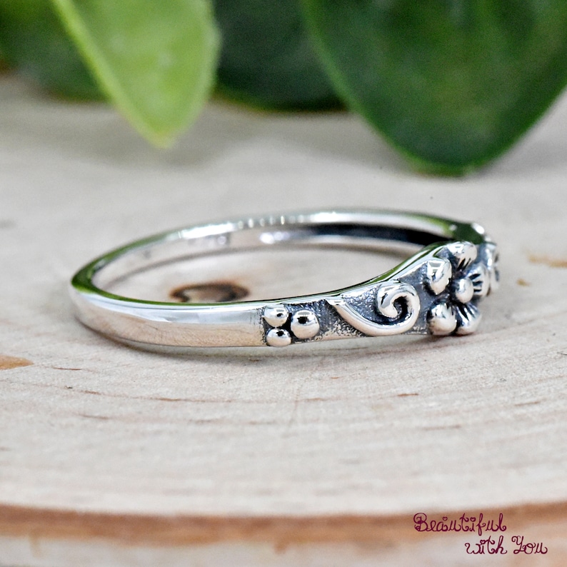 May include: A silver ring with a floral design. The ring has a delicate band with three small beads on one side and a floral design on the other side.