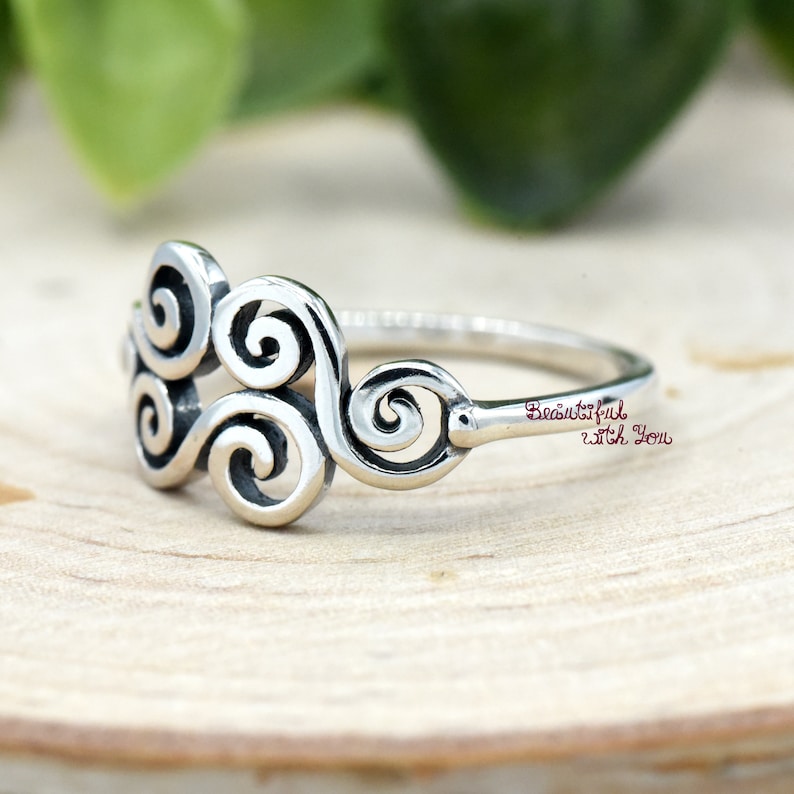 May include: Silver ring with a swirling design. The ring is on a wooden surface. The text "Beautiful with You" is engraved on the band.