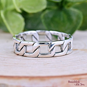 Puede incluir: Un anillo de cadena de plata con un diseño simple. El anillo está hecho de metal pulido y tiene un acabado liso.