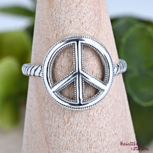 May include: A silver peace sign ring with a textured band. The peace sign is outlined with small dots.