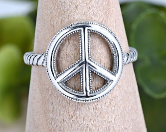 Könnte beinhalten: Ein silberner Friedenszeichenring mit einem strukturierten Band. Das Friedenszeichen ist mit kleinen Punkten umrandet.