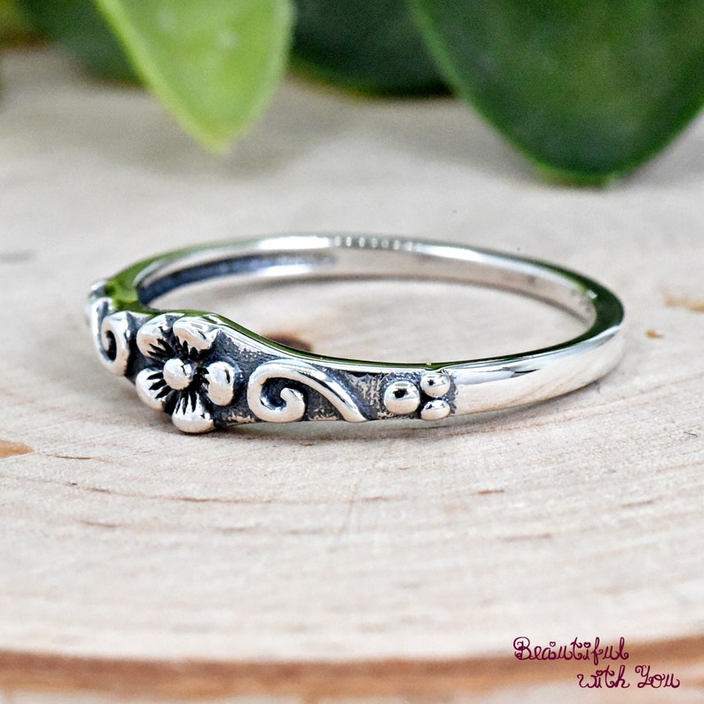 May include: A silver ring with a delicate floral design. The ring features a small flower with a swirl on either side.