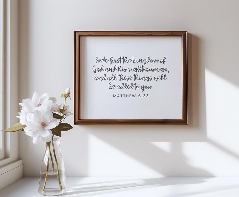 This mockup shows what this unframed Matthew 6 33 Bible verse poster could look like in a wood frame. It has a white background and gray text. It says seek first the kingdom of God ... It is shown in a minimalist and modern room.