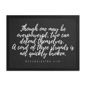 May include: A framed print with a black frame and a dark gray background. The white text reads, "Though one may be overpowered, two can defend themselves. A cord of three strands is not quickly broken." The text "ECCLESIASTES 4:12" is at the bottom.