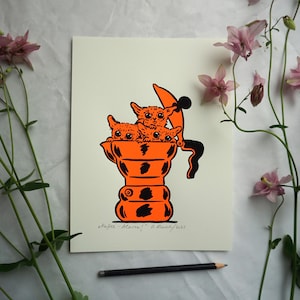 May include: An orange and black art print featuring three cartoon kittens inside a coffee pot. The print has the text "Kaffee-Alarm!" and the artist's signature. The artwork is on a cream-colored background, with pink flowers and a pencil.
