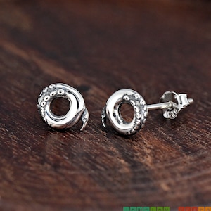 May include: A pair of silver stud earrings with a textured, circular design. The earrings are made of sterling silver and have a post-back closure.