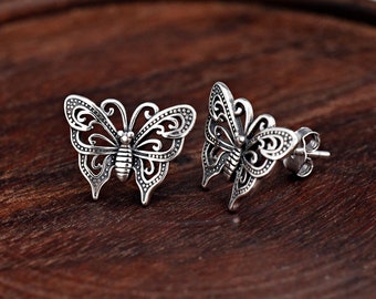 May include: A pair of silver butterfly stud earrings. The earrings feature intricate openwork designs on the wings and body. The earrings are displayed on a dark wooden surface. The text "JEWELRY SEASON" is visible in the bottom right corner.