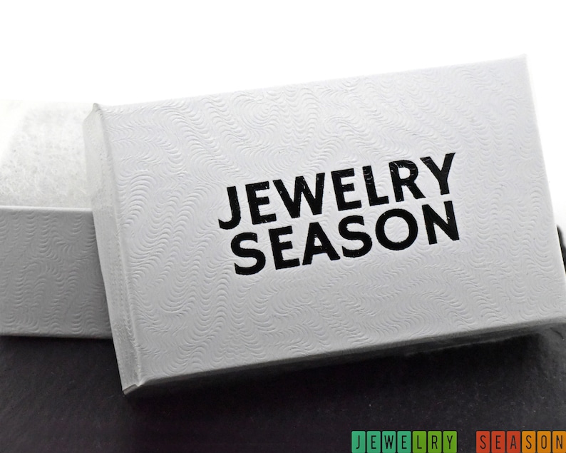 K&ouml;nnte beinhalten: Wei&szlig;e Schmuckschatulle mit einem strukturierten Deckel und dem Aufdruck "Jewelry Season" in Schwarz.