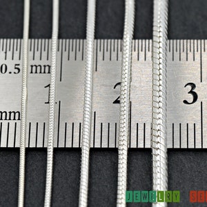 K&ouml;nnte beinhalten: Vier silberne Schlangenketten in verschiedenen Breiten liegen neben einem Lineal. Die Ketten werden in Millimetern gemessen, wobei die kleinste Kette 1 mm und die gr&ouml;&szlig;te Kette 3 mm misst.
