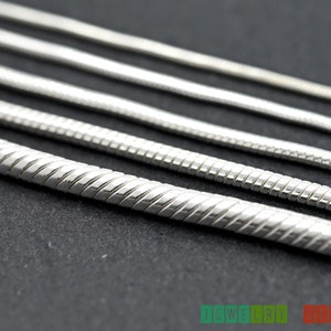 K&ouml;nnte beinhalten: Nahaufnahme einer silbernen Schlangenkettenhalskette. Die Kette besteht aus kleinen, ineinandergreifenden Gliedern, die einen glatten, flie&szlig;enden Look erzeugen.